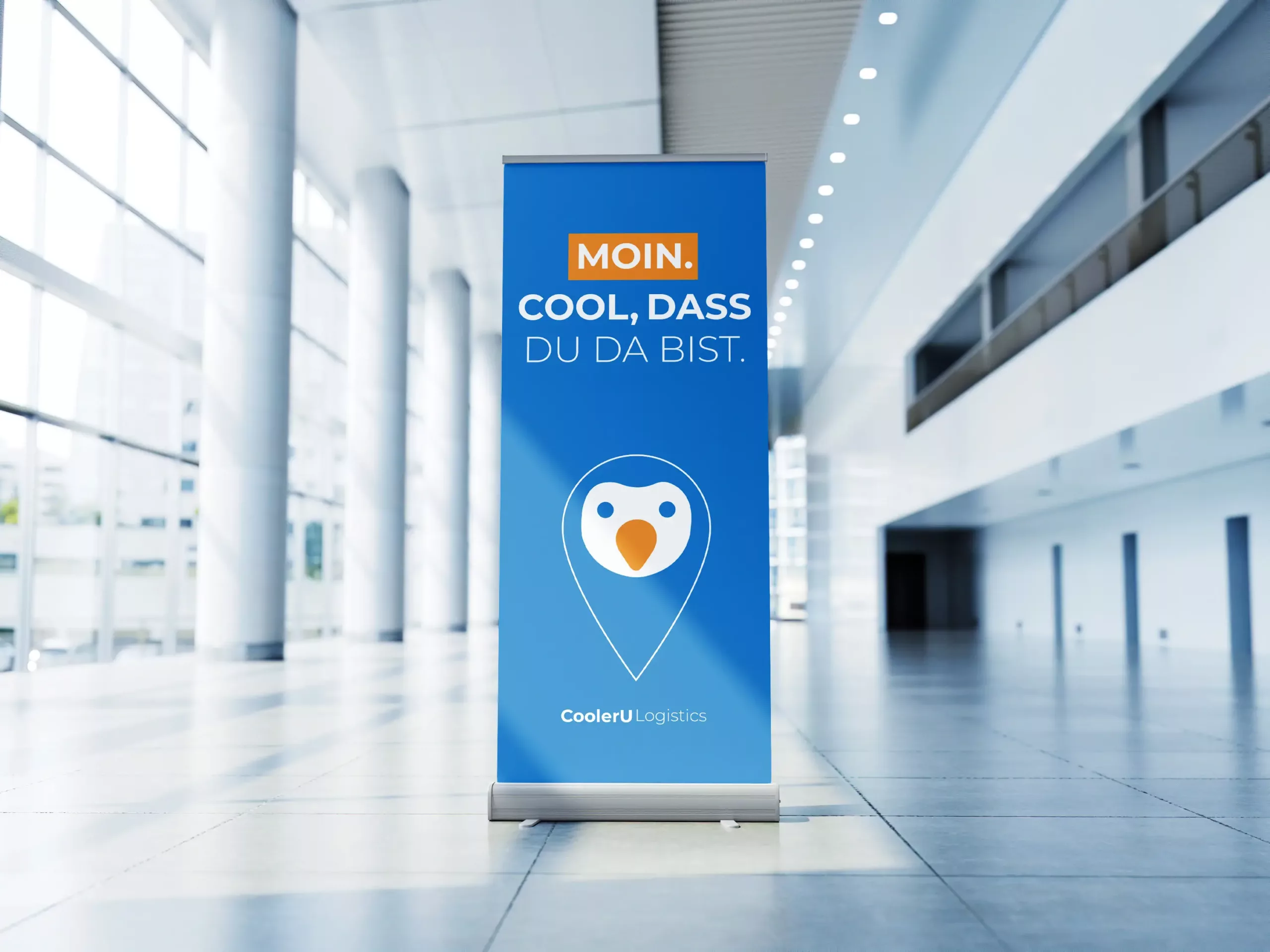 Ein blaues CoolerU Logistics-Banner mit einem Pinguin-Logo und deutschem Text steht in einer modernen, hellen, gläsernen Lobby.