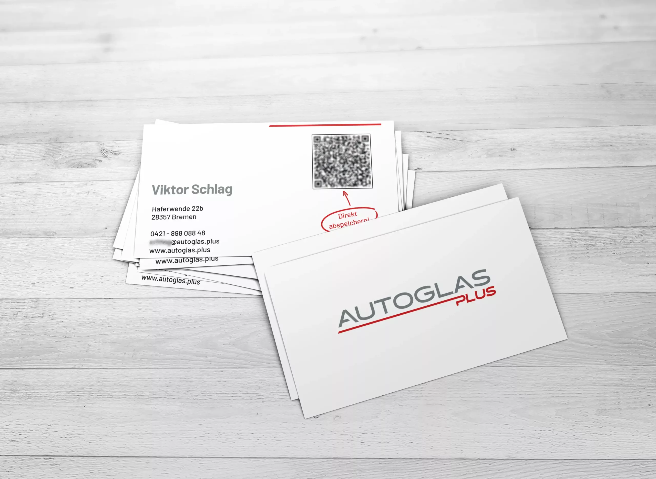 Ein Stapel Visitenkarten auf einer hellen Holzoberfläche, die auf einer Seite das AUTOGAS PLUS-Logo und auf der anderen Seite die Kontaktdaten von Viktor Schlag mit einem QR-Code zeigen.