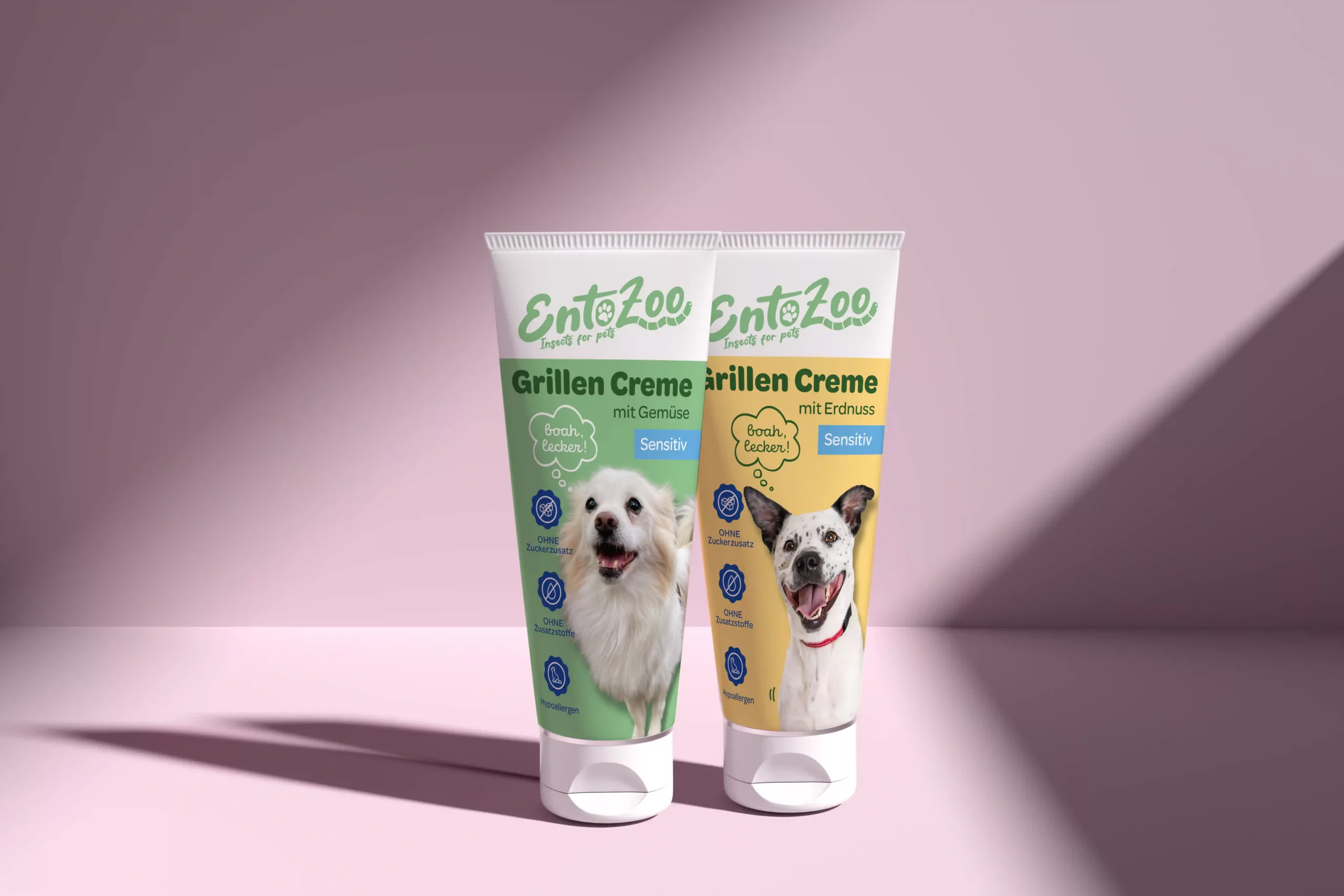 Zwei Tuben EntoZoo Grillen Creme Tiernahrung für Hunde mit Bildern von weißen Hunden und Text über Geschmack und Empfindlichkeit auf einer weißen Oberfläche mit einem Schatten.