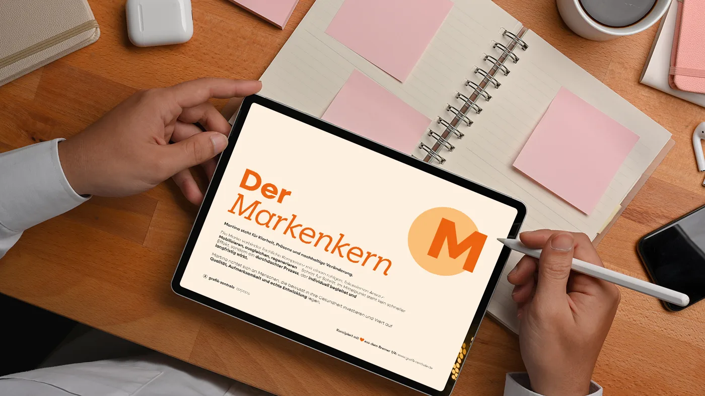 Eine Person hält ein Tablet, auf dem ein Dokument mit dem Titel "Der Markenkern" in deutscher Sprache abgebildet ist, mit Notizbüchern, Haftnotizen und Büromaterial auf einem Holztisch.