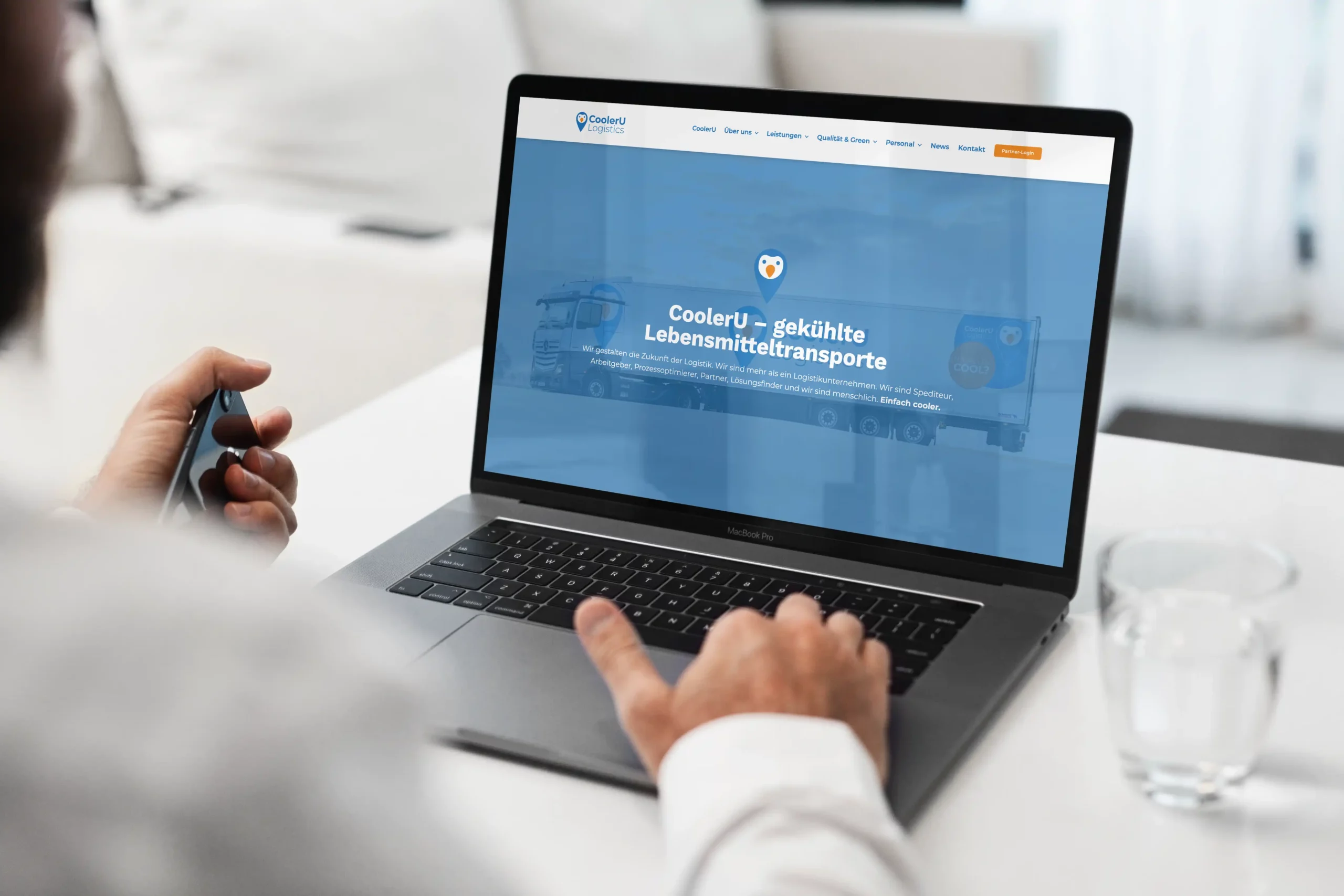 Eine Person benutzt einen Laptop, auf dem eine Website für "CoolerU - gekühlte Lebensmitteltransporte" mit einem LKW-Bild und einer blauen Kopfzeile angezeigt wird.